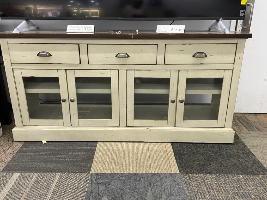 Cream tone distressed wooden TV console with four glass doors, 2 shelves, 3 drawers